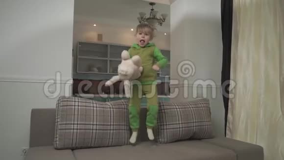 柔柔的小男孩穿着绿色睡衣在家里的沙发上跳孩子抓起枕头扔到地板上快乐视频的预览图