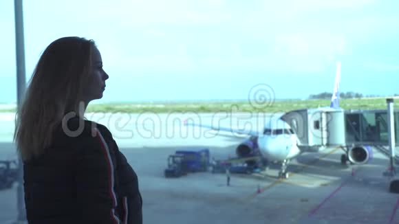 年轻的女旅行者在机场候机室等待飞机时望着窗户漂亮的女孩视频的预览图