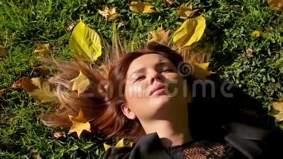 红头发的女孩躺在草地上抱着秋天落叶的公园视频的预览图