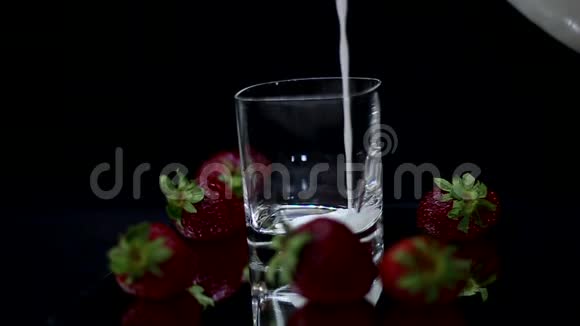 把牛奶放在杯子里在黑色背景上放新鲜的红色草莓视频的预览图