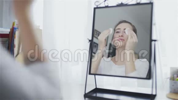美丽的女人在镜子前用棉垫洗脸视频的预览图