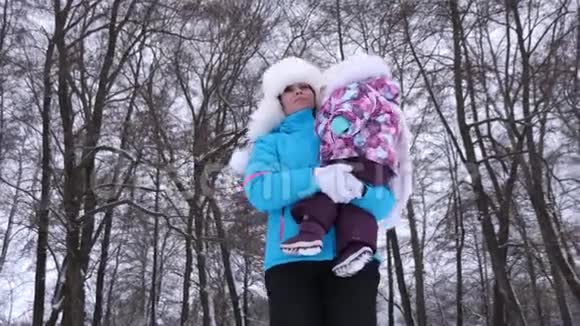 快乐的母亲抱着小女儿在冬天穿过白雪覆盖的公园与父母一起散步视频的预览图