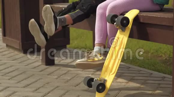 孩子们坐在长凳上移动着腿一个黄色的滑板站在旁边视频的预览图