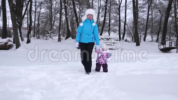 冬天妈妈在雪地公园散步时牵着她小女儿的手母亲带着孩子走视频的预览图