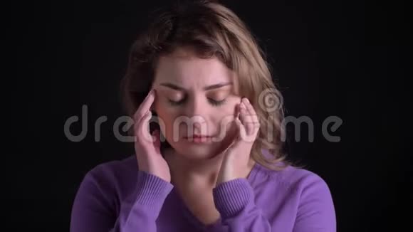 一幅悲伤的金发白种女人在黑色背景下头痛按摩的肖像视频的预览图