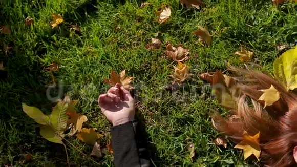 红头发的女孩躺在草地上抱着秋天落叶的公园视频的预览图