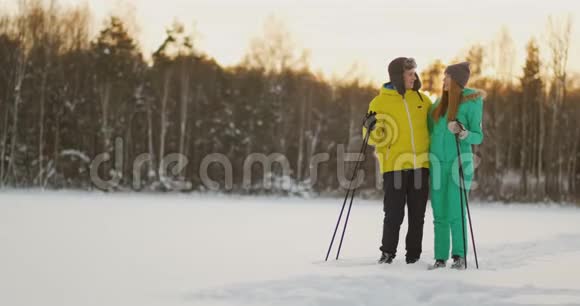 在冬天的森林里滑雪时用慈爱的眼睛看着对方一对已婚夫妇过着健康的生活方式视频的预览图