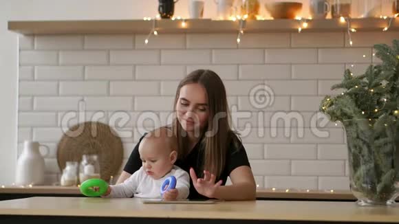 妈妈和宝宝坐在白色明亮的公寓里的桌子旁妈妈把手指按在平板电脑的屏幕上视频的预览图