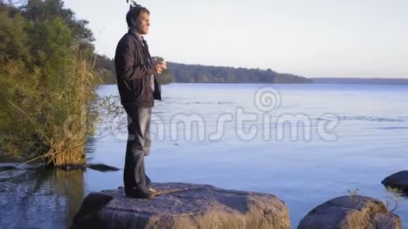 一个人站在大石头上躺在河里手里拿着一杯茶看着日落视频的预览图