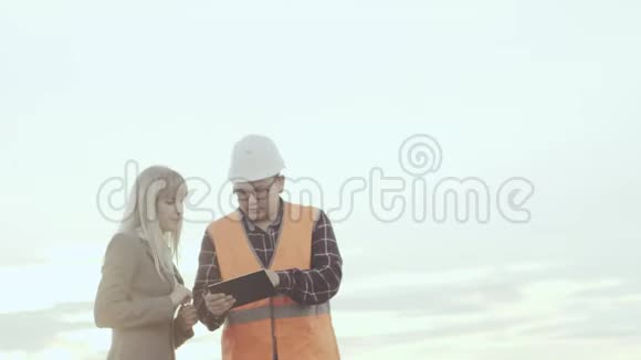 一个穿着反光背心和头盔的承包商在风车的背景下与一位商务女士进行了交易视频的预览图