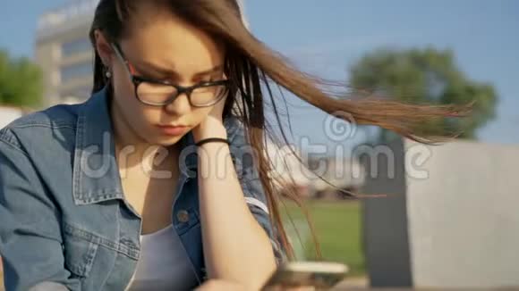 一个戴眼镜的年轻女孩坐在街上用耳机听音乐手里拿着电话的女孩视频的预览图