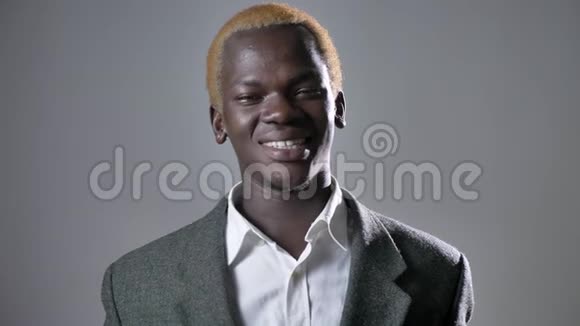 年轻快乐的金发非洲男人在镜头前微笑在灰色背景下与人接触成功的商人视频的预览图