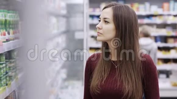 在购物中心杂货店的冰箱里选择酸奶的年轻女人视频的预览图