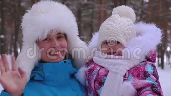 妈妈挺直了小女儿的帽子微笑着挥动她的手快乐的女人带着孩子在冬天散步笑母亲视频的预览图