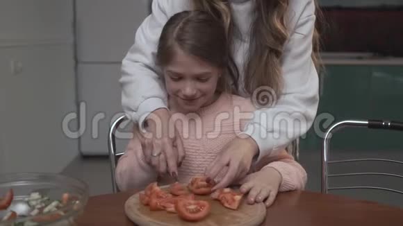 年长的女孩教年轻的女孩切西红柿做沙拉两个姐妹坐在那儿一边吃蔬菜沙拉视频的预览图