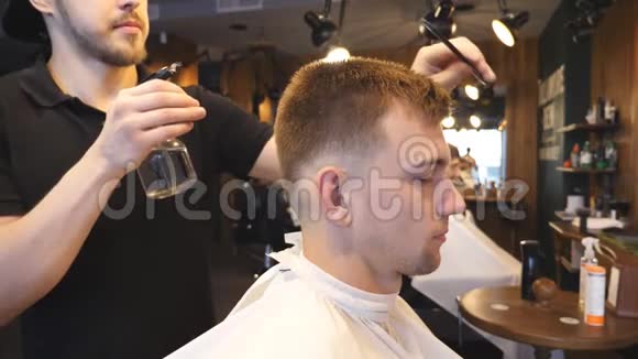 年轻的发型师在理发店剪下头发后从喷雾器上喷洒水理发师梳头视频的预览图