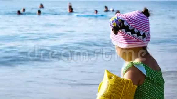 小可爱的女孩坐在海滩上把鹅卵石扔进水里视频的预览图