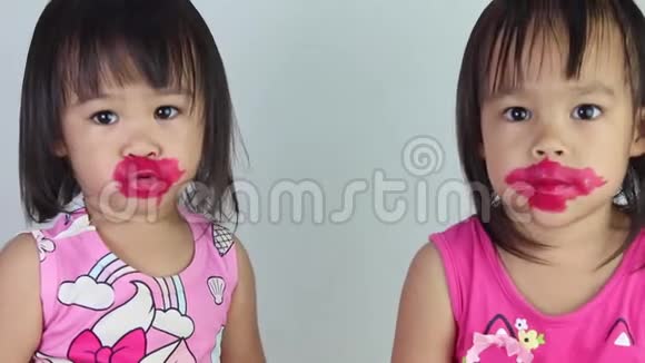 亚洲小女孩在白色背景上为妹妹涂红色口红视频的预览图