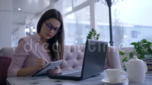 远程学习年轻女子在笔记本电脑上进行在线交流并在咖啡馆的餐桌上展示笔记本视频的预览图