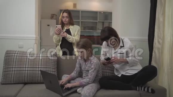 两个姐姐在手机上发短信小女孩坐在房间里的沙发上用笔记本电脑打字家庭视频的预览图