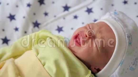 一个刚出生的婴儿穿着绿色的婴儿衣服和帽子哭着躺在床上特写视频的预览图