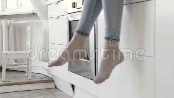 靠近女人的腿悬挂白色厨房抽屉和烤箱的背景行动穿牛仔裤的女人视频的预览图