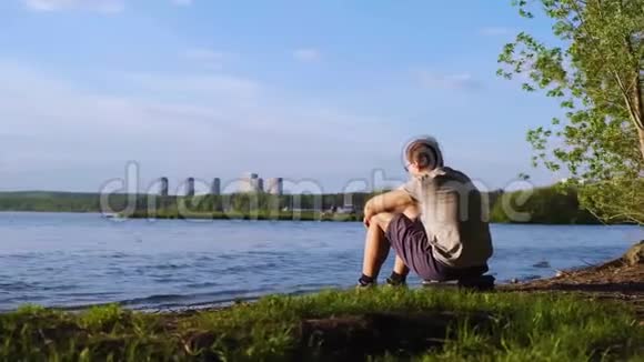 年轻人坐在城市背景的河岸上库存录像人坐在河边欣赏大自然的景色视频的预览图