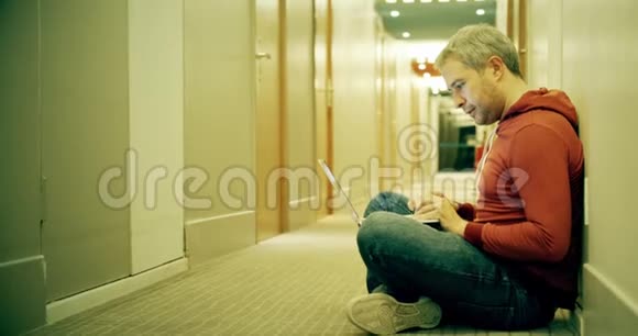 穿休闲服装的聪明灰发男人在酒店走廊里用笔记本电脑视频的预览图