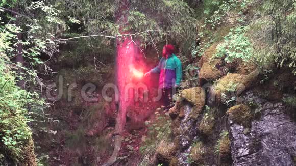 徒步旅行者穿着鲜艳的衣服观察悬崖上的绿色植物手持燃烧的红色信号耀斑股票视频的预览图