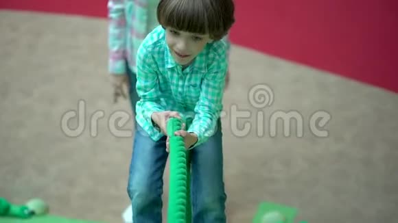 可爱快乐的小男孩玩耍在操场上爬上一个绳梯在操场上孩子在商场里爬绳子视频的预览图