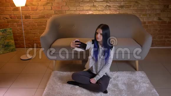 年轻有魅力的白种人女性的特写上自拍坐在地板上微笑的特写照片视频的预览图