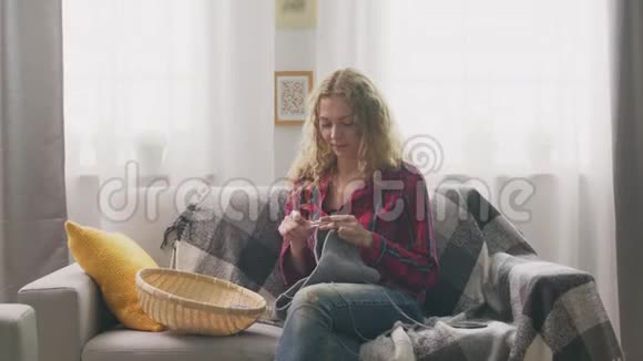 放大女人坐在沙发上在家里编织在镜头里看视频的预览图