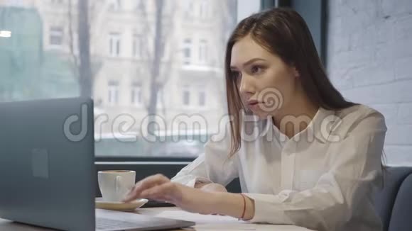 不高兴的女人用她的笔记本电脑坐在咖啡馆的桌子上坐在靠近窗户的沙发上用电脑工作的女孩视频的预览图