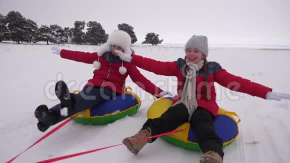 快乐的孩子在雪的路上骑雪快乐地笑女孩们在冬天雪橇微笑着快乐视频的预览图