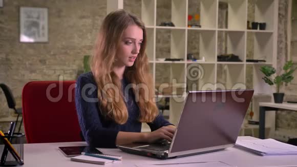 忙碌的白种人女商人在办公室里用笔记本电脑工作的肖像在平板电脑上收到通知视频的预览图