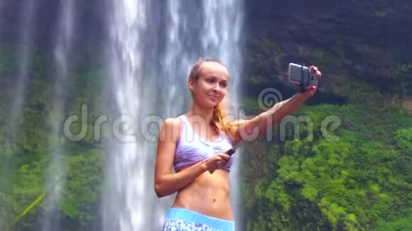 扎着马尾辫的女孩在美丽的瀑布上自拍视频的预览图