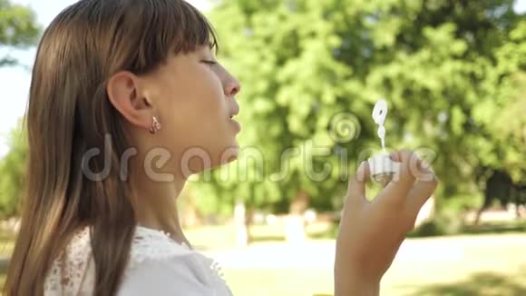 美丽的女孩在春天夏天和微笑的公园里吹肥皂泡特写镜头在公园里玩的年轻女孩视频的预览图