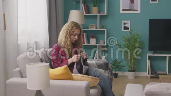 年轻女子坐在沙发上看着智能手机上的编织教程视频的预览图