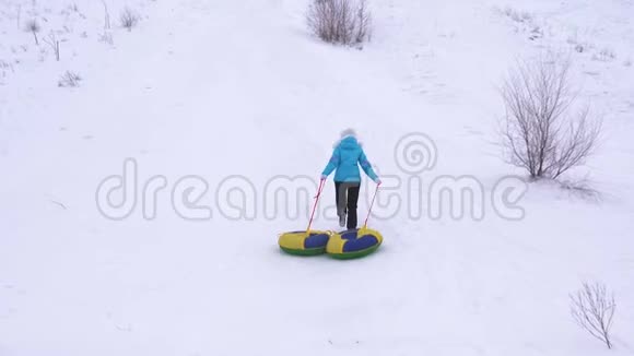 女孩爬上高高的雪山手里拿着雪碟女人在冬天玩雪橇山区度假胜地视频的预览图