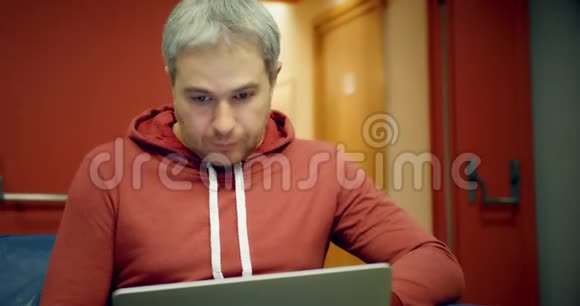 穿休闲服装的年轻聪明灰发男子在大厅里用笔记本电脑视频的预览图
