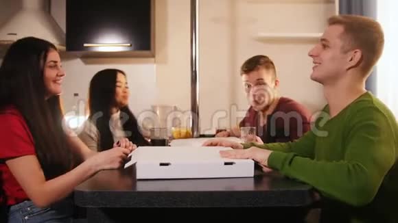 四个饥饿的年轻朋友在厨房打开披萨盒拿一块视频的预览图