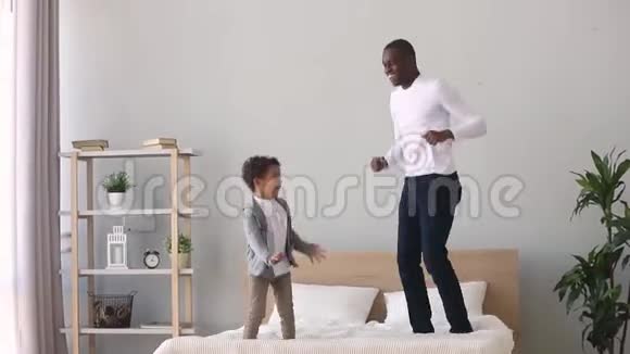 快乐无忧无虑的非洲父亲和儿子在床上跳跃视频的预览图