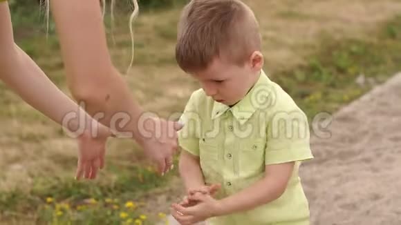 一个小男孩在公园里和他的母亲散步他刷掉了他肮脏的手视频的预览图