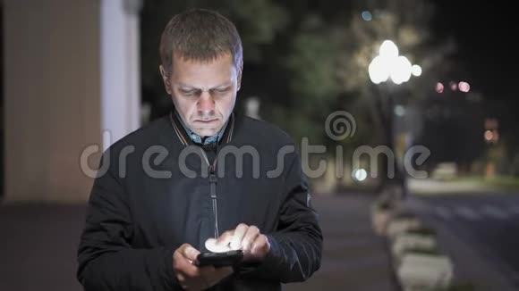 夜城中站在智能手机上通过联系人的男士特写视频的预览图