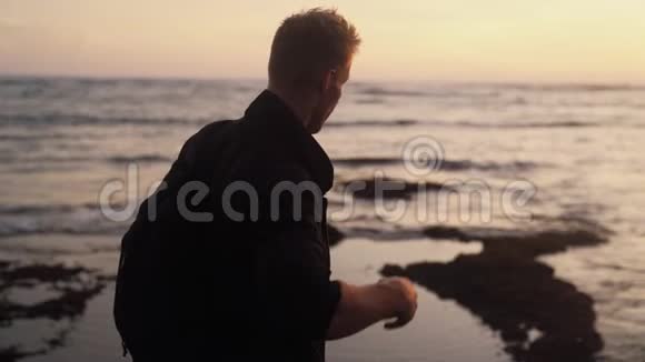 背面的人与背包观看金色日落在海洋海滩慢动作稳定射击视频的预览图
