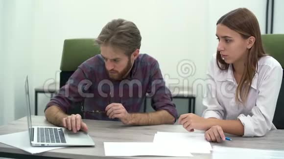 蓄胡子的老板手里拿着眼镜指着一个笔记本电脑屏幕同时把注意力集中在他的员工身上视频的预览图