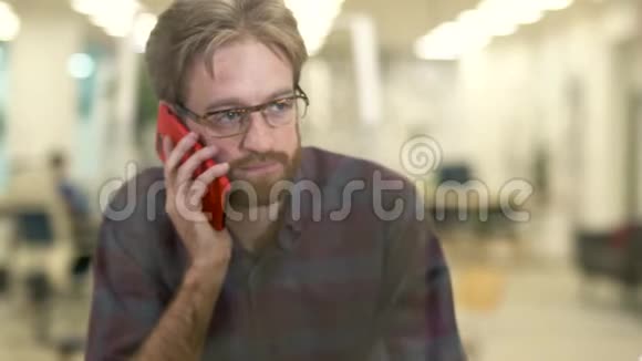 戴着眼镜穿着休闲格子衬衫的胡子笑眯眯的家伙在手机上说话视频的预览图
