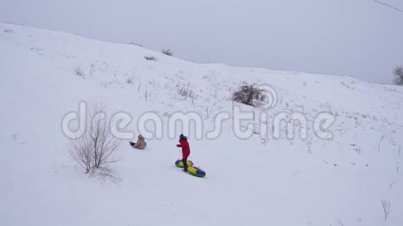 快乐的女孩在雪碟上从雪山上滚动女孩手里拿着雪碟上雪山视频的预览图
