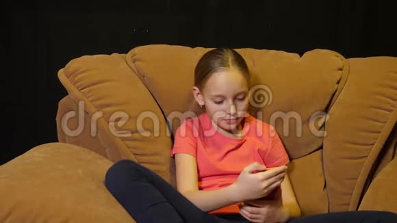 年轻少女坐在舒适的椅子上在黑色背景下使用手机视频的预览图