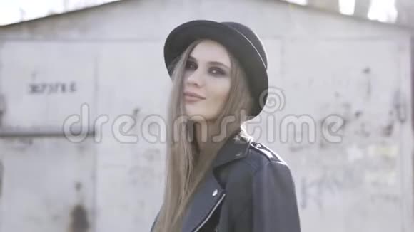 性感的现代时髦女人戴着帽子穿着时髦的黑色夹克呆在一座老式建筑附近的街道上行动视频的预览图